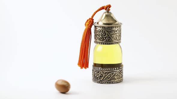 Single argan nut is rolling towards a bottle of Argan Oil 