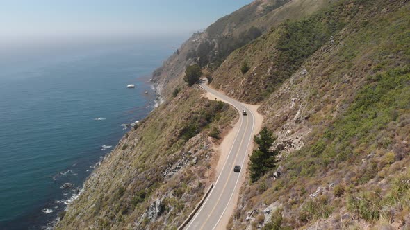Drone flies behind cars on narrow highway on the cliffs of Big Sur