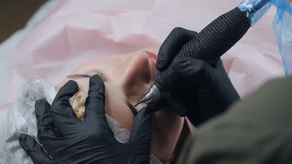 Hands of a Beautician in Black Gloves Doing Permanent Makeup on Female Eyebrows