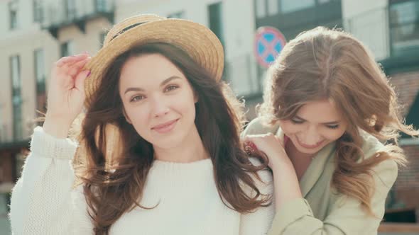 Two young beautiful smiling hipster girls in trendy clothes posing outdoors