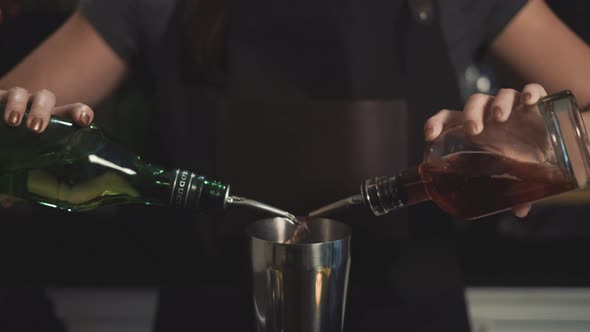Bartender pouring two liquor bottles into cocktail shaker, close up.