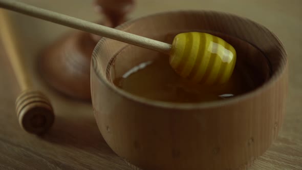 Honey with Wooden Honey Dipper in Wooden Bowl on Wooden Table