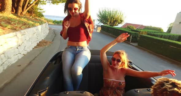Beautiful brunette sitting on hood of convertible dancing riding with friends