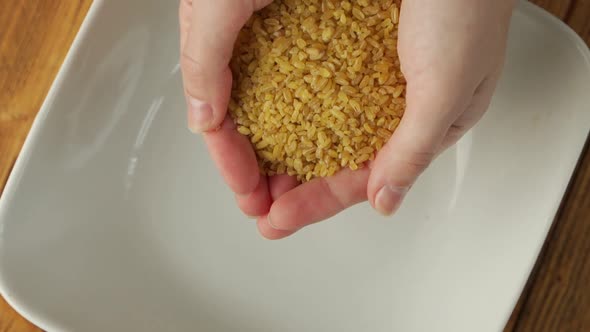 Closeup of a Woman's Hands Spilling Out Dried Yellow Bulgur Wheat Grains Into a Plate Slow Motion