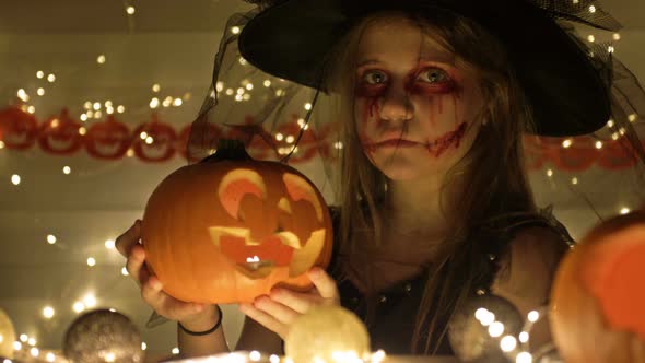 Portrait of a Teenage Girl Dressed As a Witch with Scary Makeup on Her Face. The Girl Holds a Jack-o