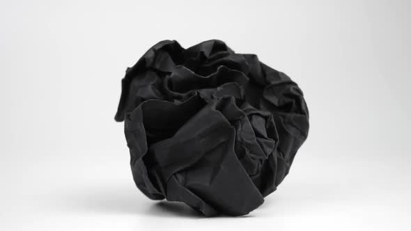 A black crumpled paper wad falls and rolls on a white surface