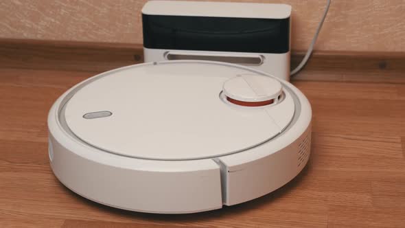 White Robotic Vacuum Cleaner Finishes Cleaning And Drives to Its Charging Station