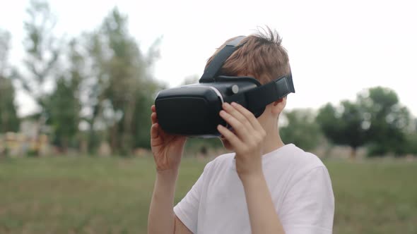 Happy Boy in Virtual Reality Glasses Plays Video Games Outdoors