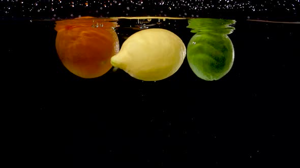 Colorful citrus fruits being dropped into water in slow motion.