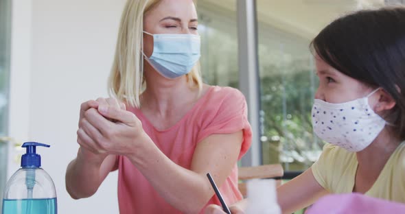 Woman wearing face mask sanitizing her hands at home