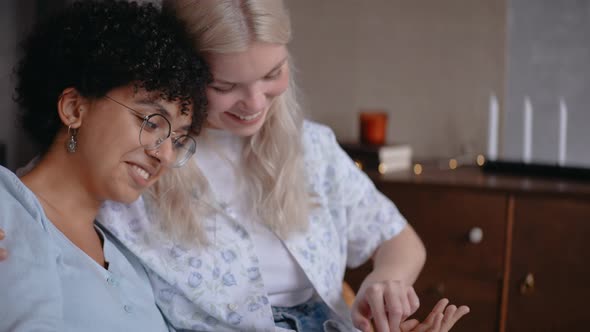 Girls Look at Lines on Their Hands Laughing While Sitting on the Couch