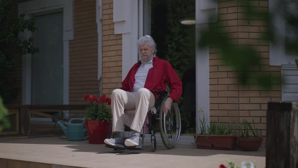 Positive Bearded Disabled Man Rolling Wheelchair on Porch in Slow Motion Admiring Sunlight Outdoors