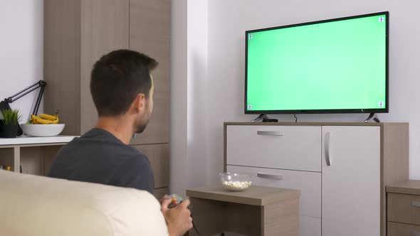Man Playing a Video Game on the Console in Front of Green Mock-up Screen on Big Plasma TV