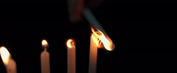 Person lighting up Hanukkah menorah candles in a dark room, slow motion