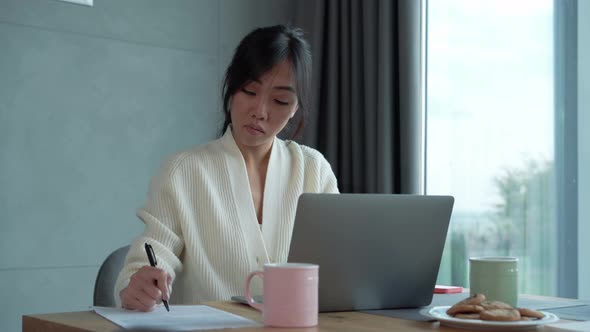 Pensive Asian woman working on laptop