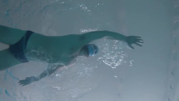 A Man Swims in a Pool Underwater in a Protective Medical Mask