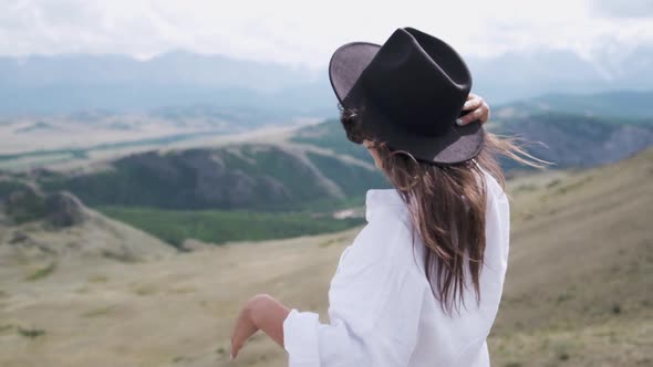 Attractive Brunette in a Hat and White Shirt Is Enjoying Nature in the Mountains. Beautiful Young