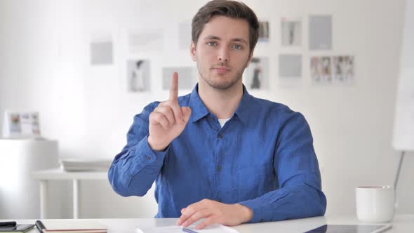 Young Man Rejecting Offer while Sitting at Workplace