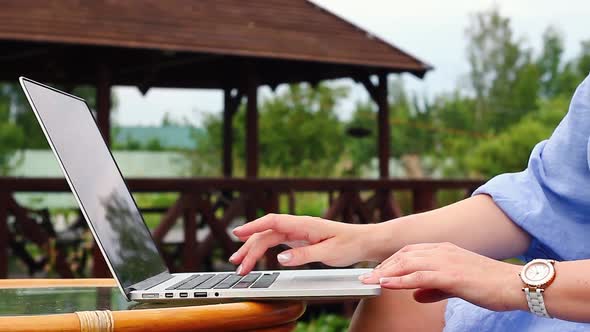 Woman Sits in Nature at the Dinner Table and Works at a Light Laptop with a Clock on Her Hand