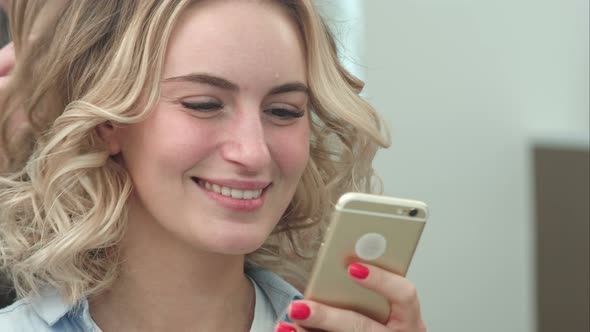 Woman Having Hair Styling in Salon While Browsing the Internet on Her Mobile Phone, Smiling