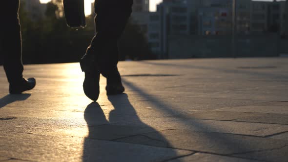 Feet of Two Businessmen Walking in City Street with Sun Flare at Background. Business Men Commute