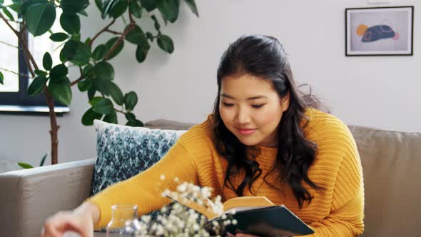 Asian Woman Reads Book and Drinks Water at Home