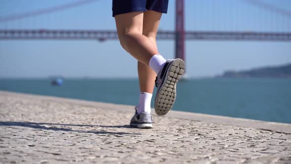 Legs of Young Sportsman Running on Pavement at Riverside