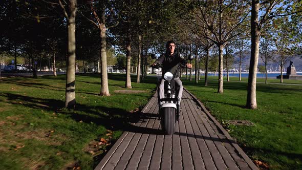 Male on electric scooter is riding through public park at sunny morning