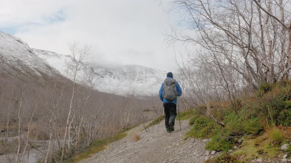 A Middle-aged Man Walking Along a Mountain Path with a Backpack