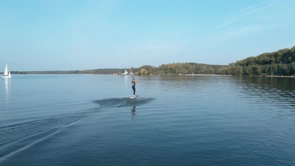 Man Riding on a Hydrofoil Surfboard and Falling in Large Blue Lake on Sunny Day