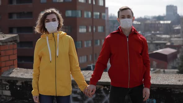 Virus Epidemic, Woman and Man in Surgical Masks Holding Hands on the Roof of City