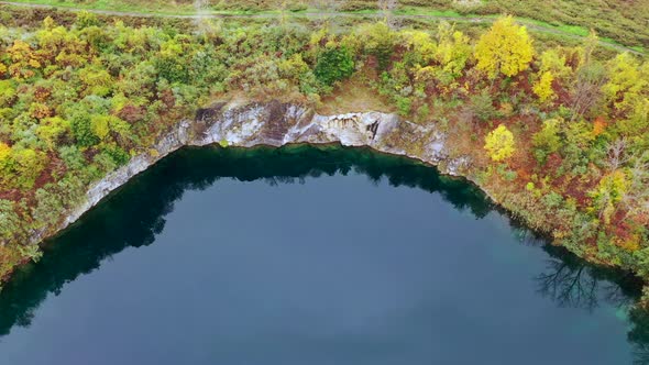 A top down view over a quarry filled with green water. The camera slowly dolly in while tilted down