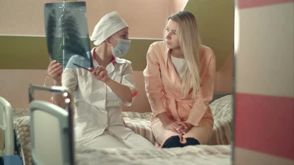 Professional Doctor Holding X-ray and Talking To Young Female Patient Sitting on Bed