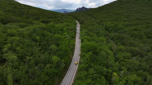 A Car Drives Down a Paved Road in a Mountainous Area That Cuts Through a Forest
