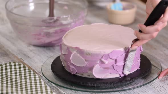 The process of decorating a cake with purple cream cover. 