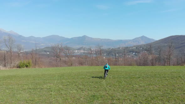 Aerial slow motion: man having fun by riding mountain bike in the grass on sunny day, scenic alpine