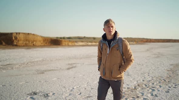 Slow Motion Adult Man Traveler in Casual Wear Walking Along White Salty Beach and Admiring Sunrise