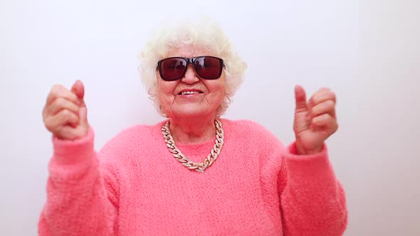 Portrait of Funny Amazed Surprised Senior Blonde Woman in Sun Glasses and Pink Sweater on White