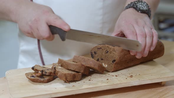 Baker is Cutting Baked Dutch Bread with Raisins and Dried Apricots with Knife