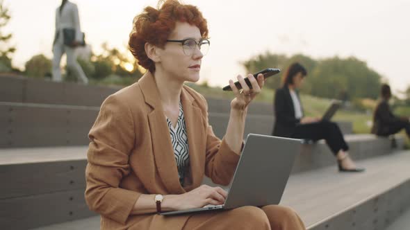 Businesswoman Recording Voice Message on Phone Outdoors