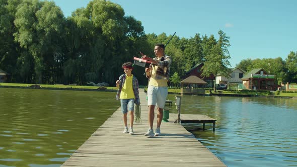 Positive Black Father and Teenage Son with Fishing Rods Going for Angling on Pond