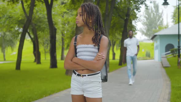 Portrait of Charming African American Girl Waiting Brother in Summer Park. Cute Sister with Pigtails