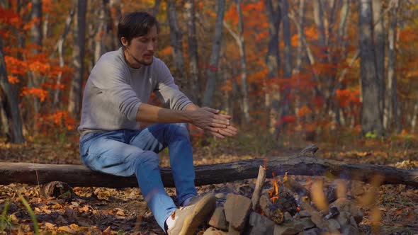 Young Man Sitting By a Bonfire in a Cold Autumn Forest. Autumn Vacation Concept