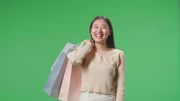 Happy Asian Shopping Woman Holding Shopping Bags Up While Standing In Front Of Green Screen