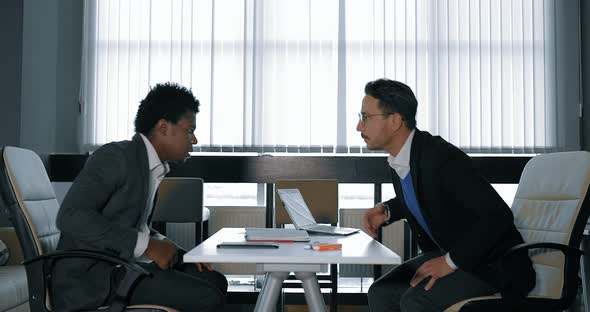 Two Young Businessman Talking at Desk in Office
