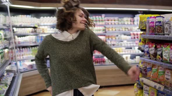 Portrait of Young Woman with Shirt Curly Hair Dancing Standing at Grocery Store Aisle
