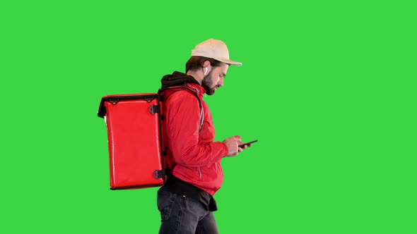 Caucasian Delivery Man Wearing Red Uniform Walking and Using Smartphone on a Green Screen Chroma Key