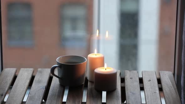 Two candles and cup of coffee on wooden table next to a window