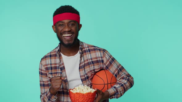 Bearded African American Young Man Basketball Fan Holding Ball Doing Winner Gesture Dancing Alone