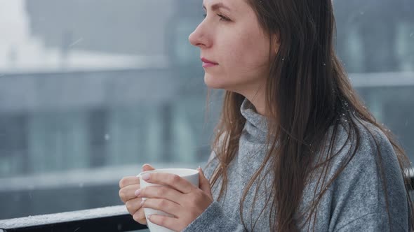 Woman Stays on Balcony During Snowfall with Cup of Hot Coffee or Tea